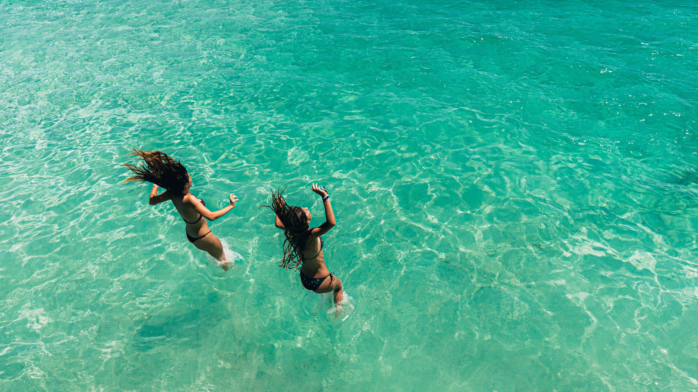 Dos chicas saltando a un mar turquesa